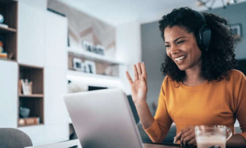 a woman smiling and waving at a computer